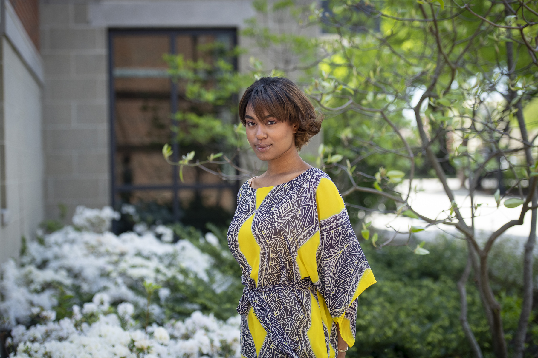 Haya Hamid standing in front of a dogwood tree wearing a yellow and gray patterned dress
